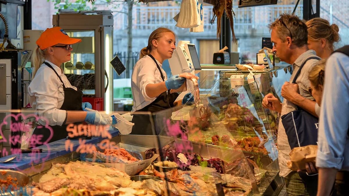 People ordering food at a busy indoor market stall in Copenhagen.