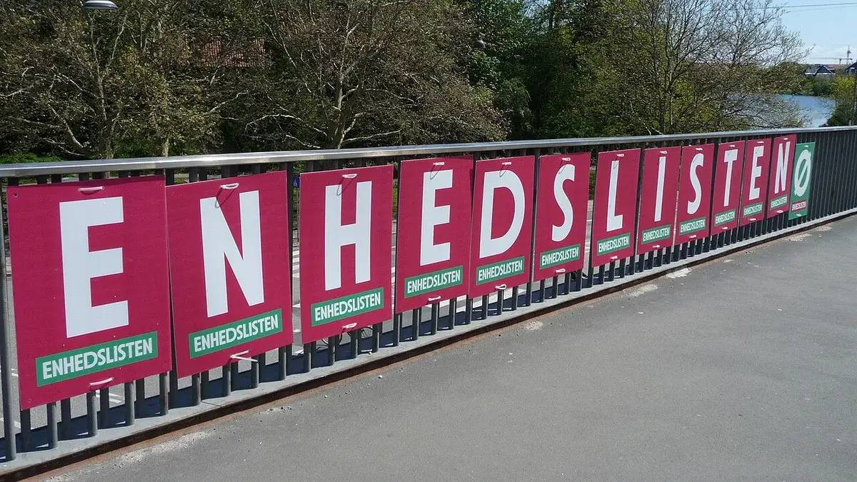 Enhedslisten political posters displayed along a railing outdoors near trees and water.