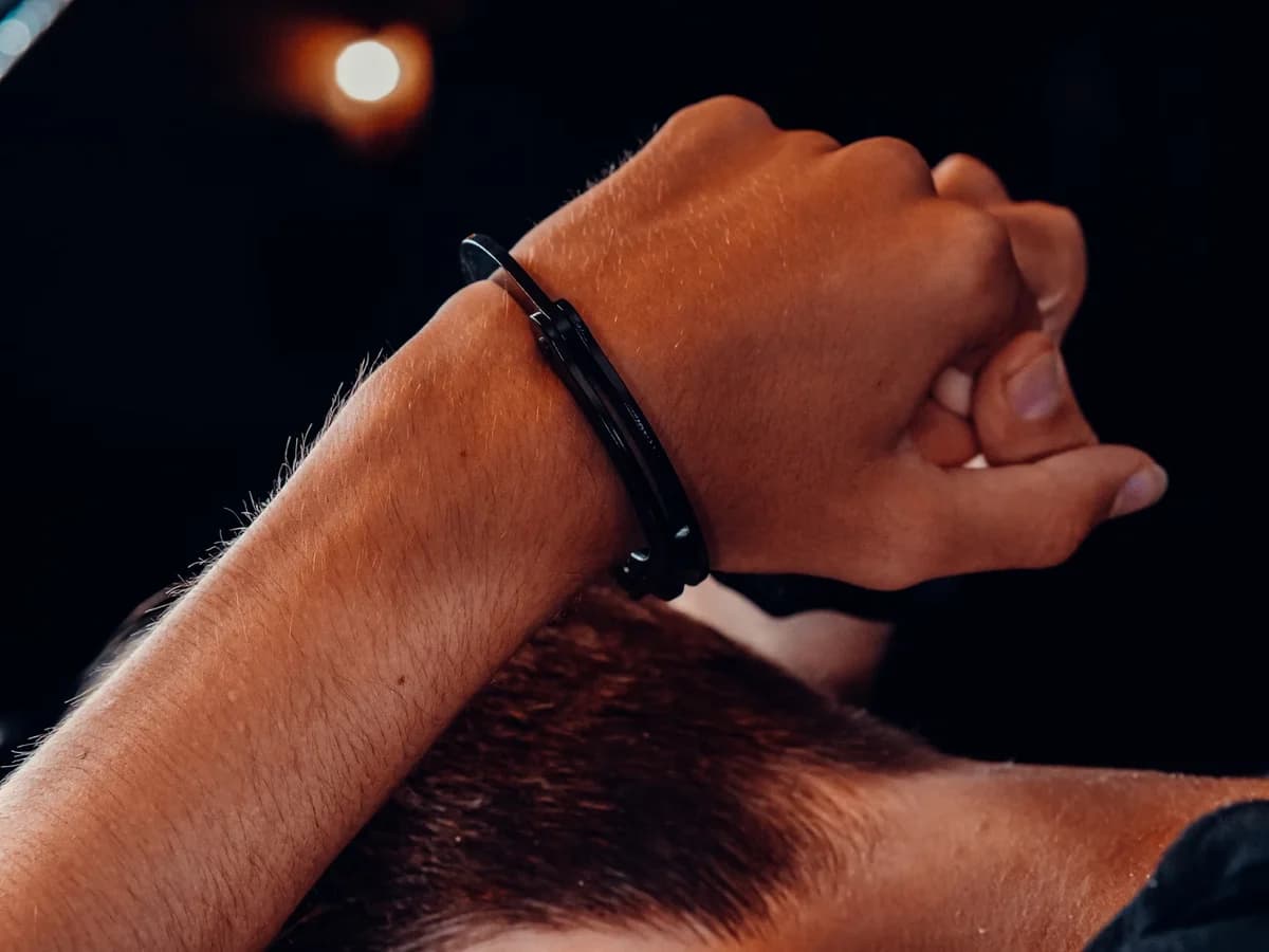 Close-up of a wrist with a black zip-tie-like restraint against a dark background.