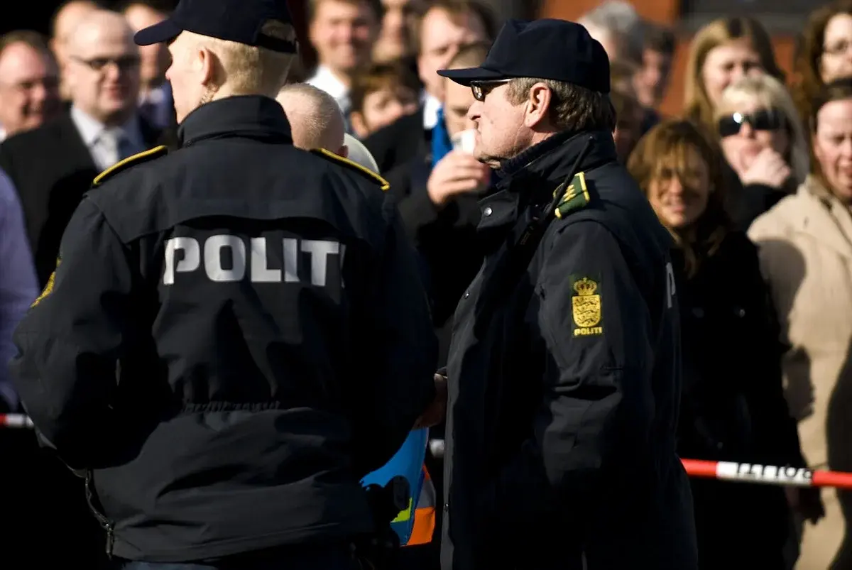 Two Danish police officers stand in front of a crowd at a public event.