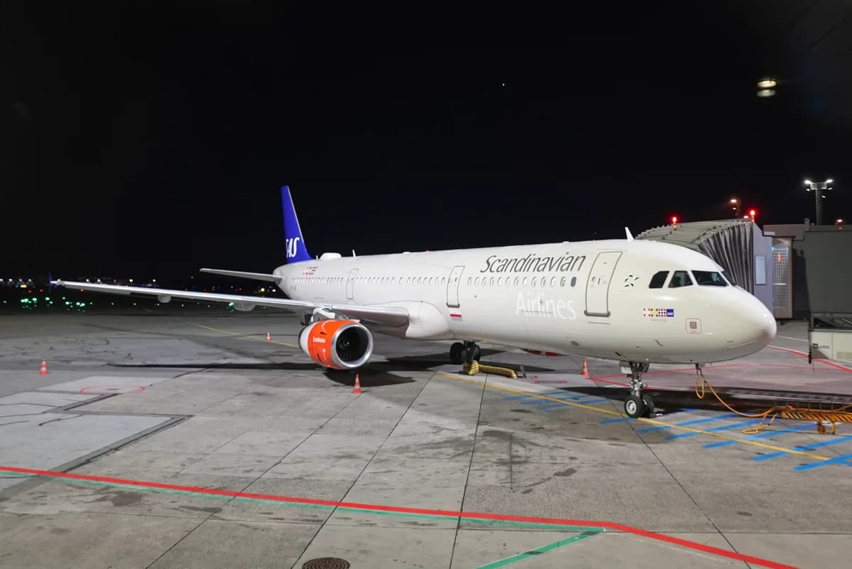 An SAS Airbus A321-200 parked at a gate at night.