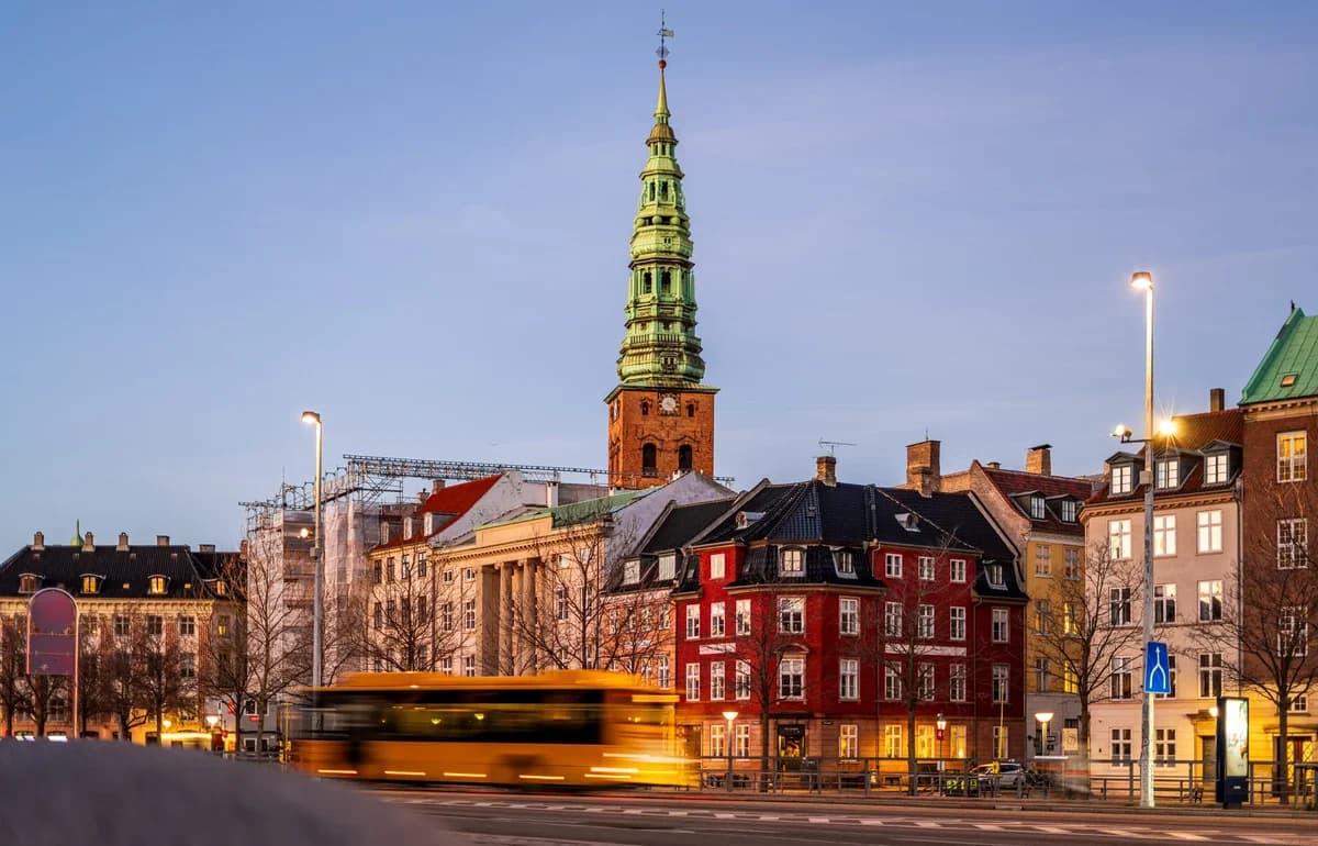 Dusk view of central Copenhagen with historic buildings and a yellow bus passing by.