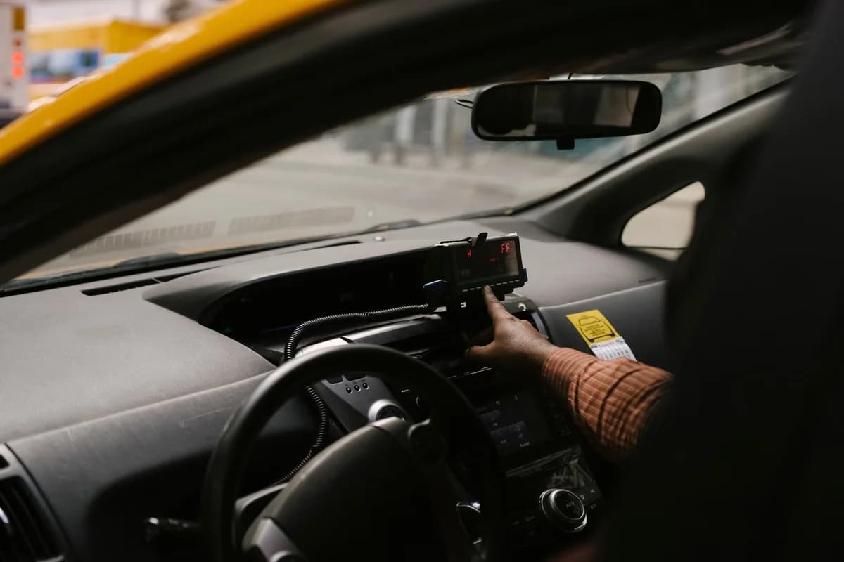 A Black male driver reaches toward a GPS device mounted on the dashboard of a car.