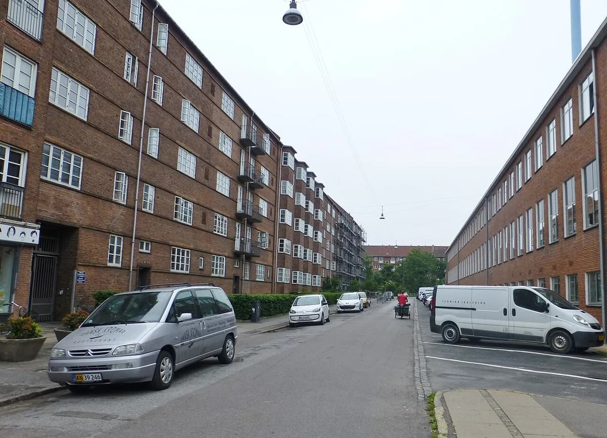 A residential street lined with brick apartment buildings and parked cars in Copenhagen.