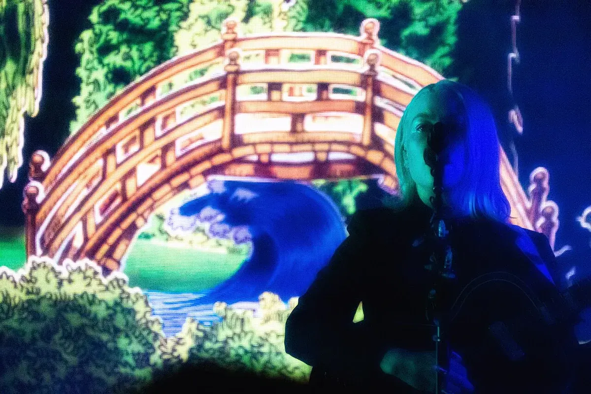 Phoebe Bridgers performing on stage with a colorful backdrop.