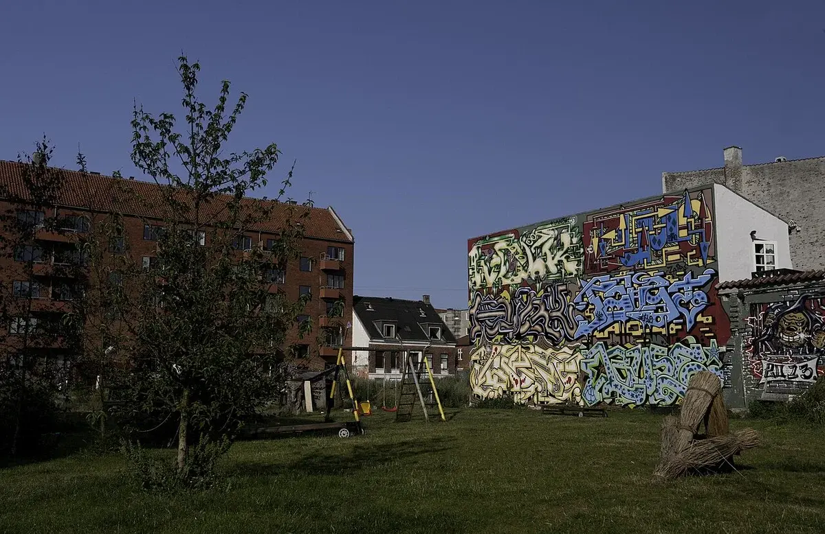 A small grassy urban park with a swing set and graffiti-covered walls.