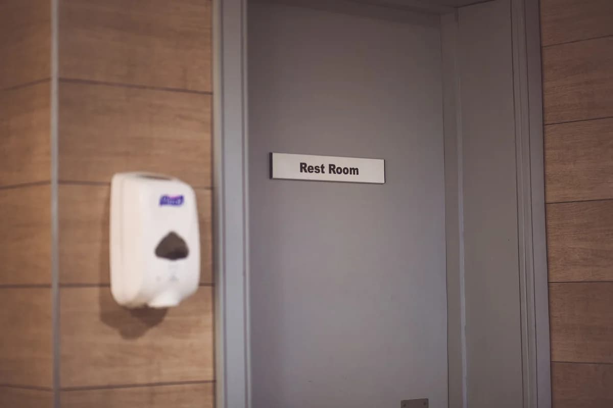 Soap dispenser next to a restroom sign on a door