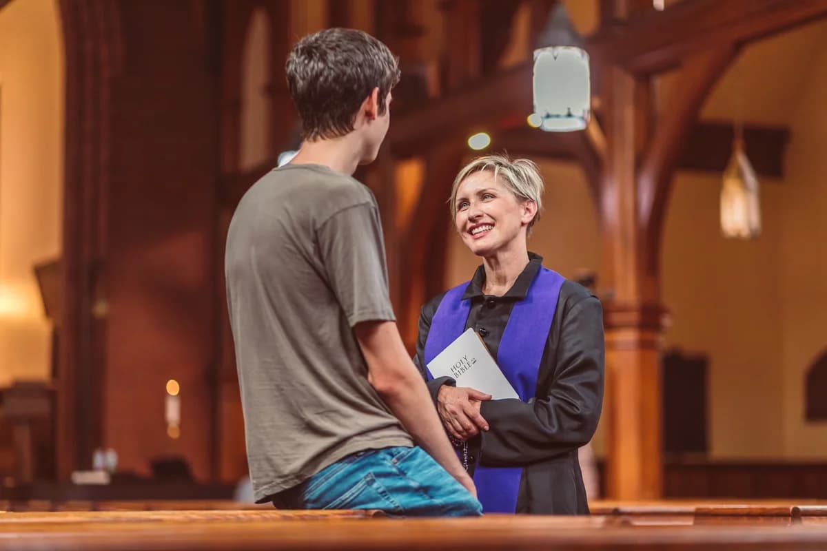 A priest smiles while talking with a young man in a church.