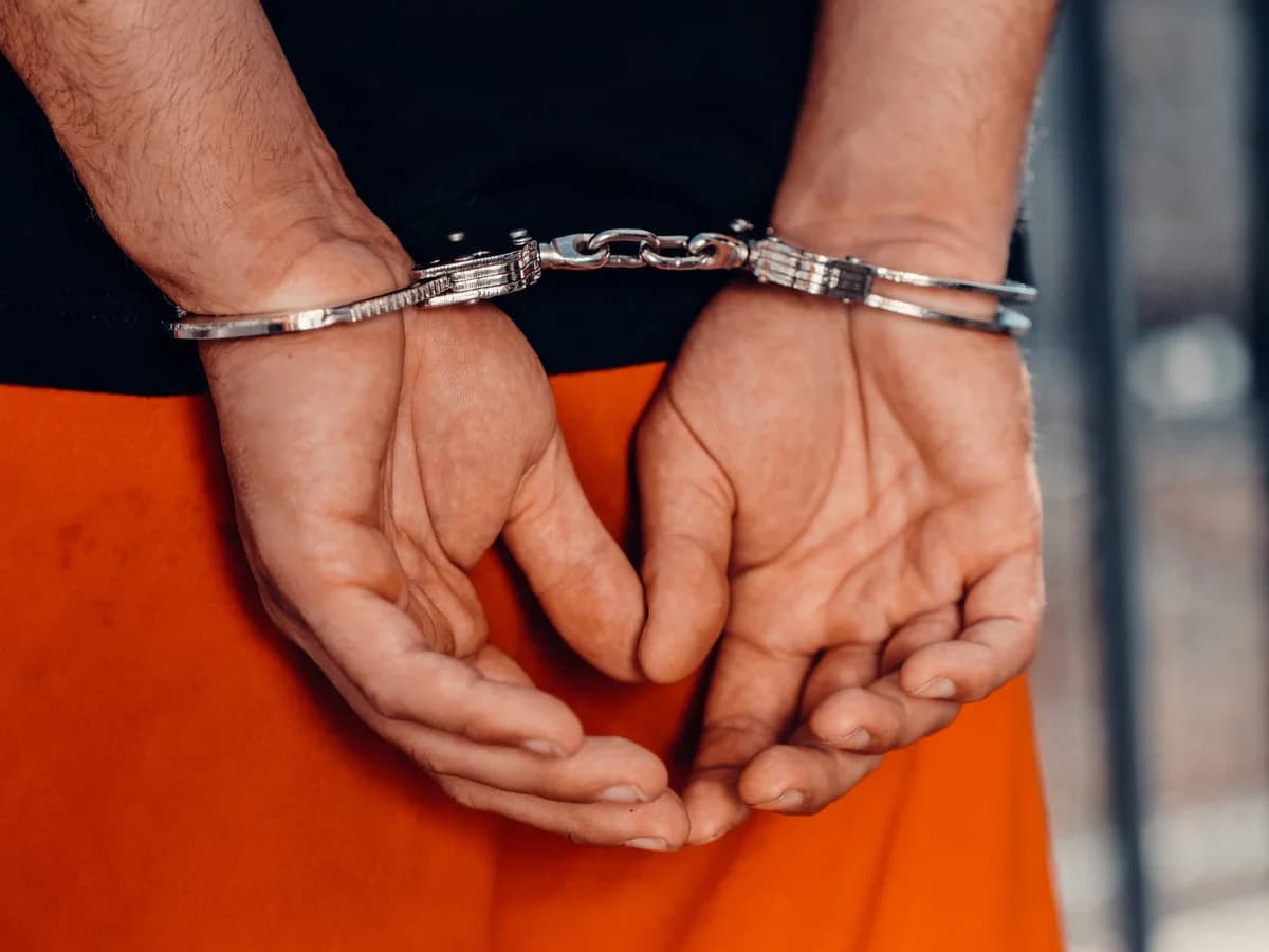 Hands cuffed behind back in handcuffs with orange pants visible