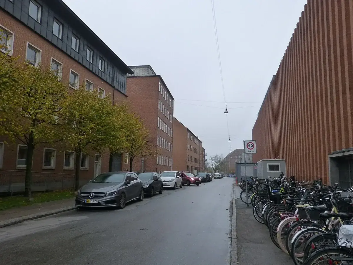 Quiet street in Copenhagen with apartment buildings, parked cars, and rows of bicycles.