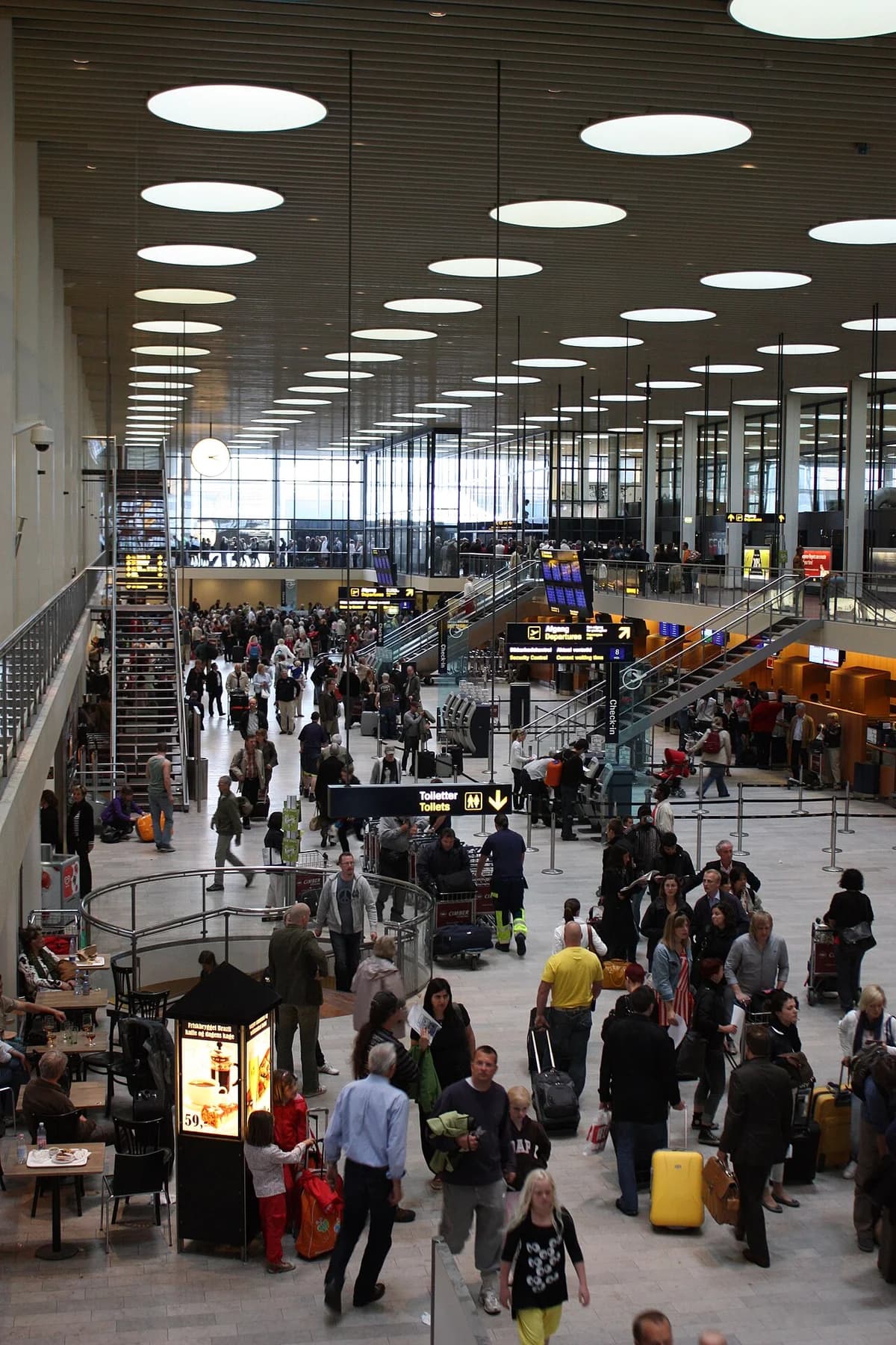 Busy airport terminal with travelers, check-in signs, and escalators.