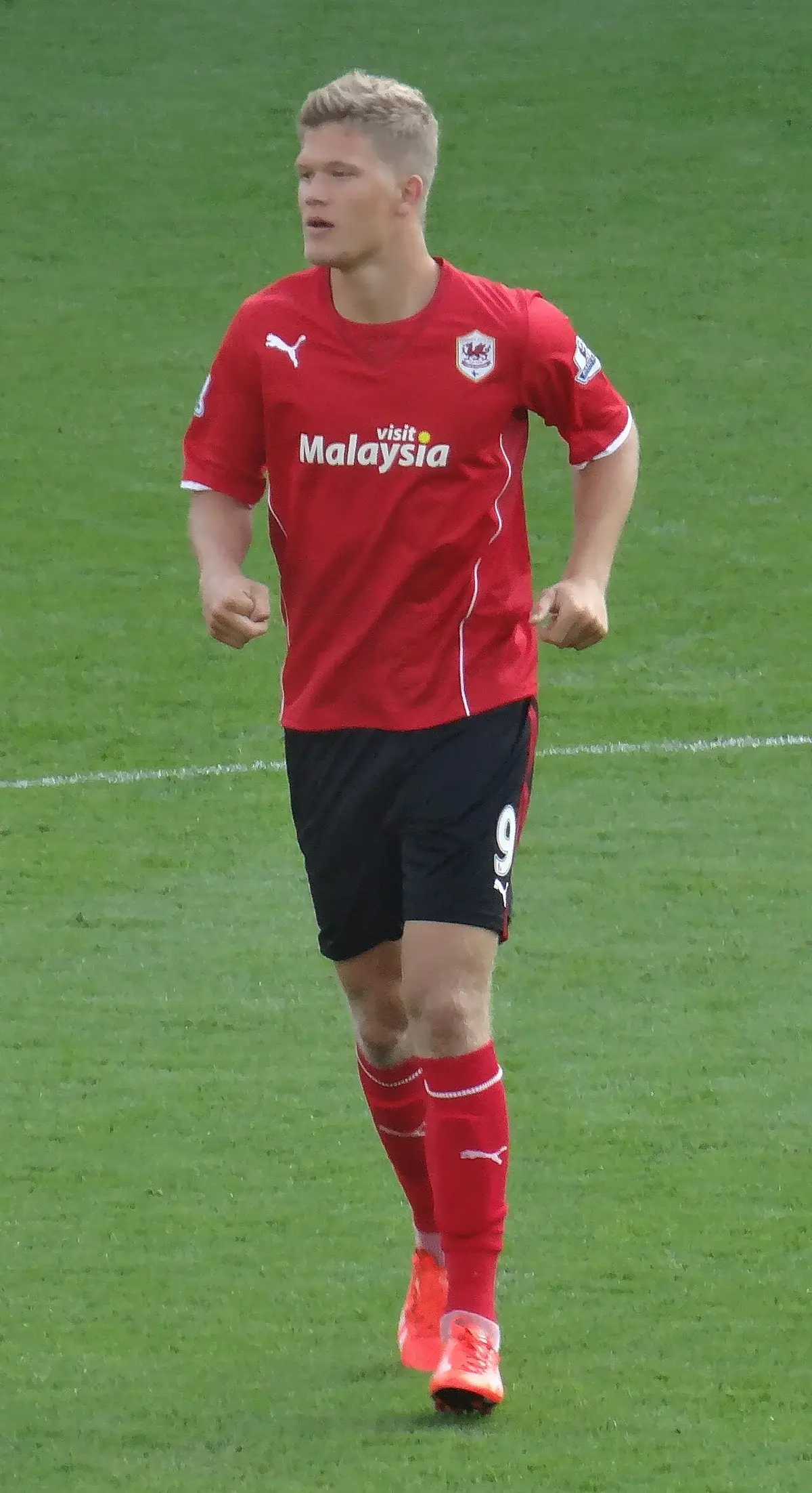 Andreas Cornelius running on a soccer field in a red Cardiff City jersey.