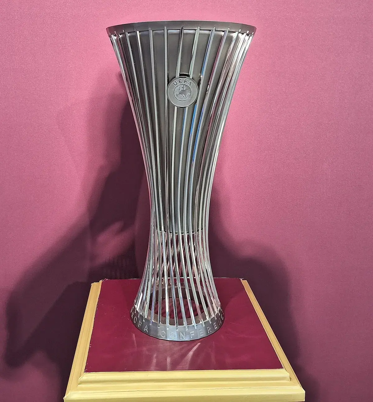 The UEFA Europa Conference League trophy on display against a pink background.
