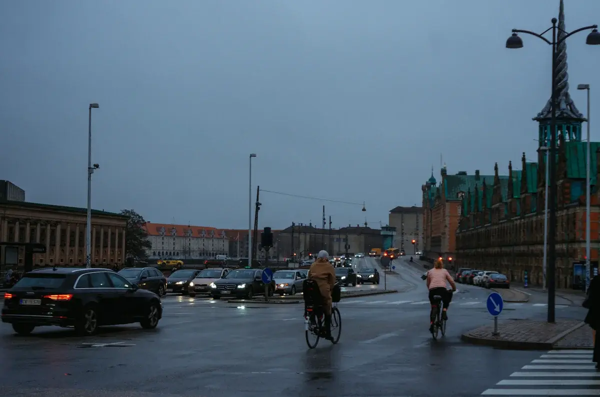 A wet Copenhagen street with cars and cyclists at dusk.