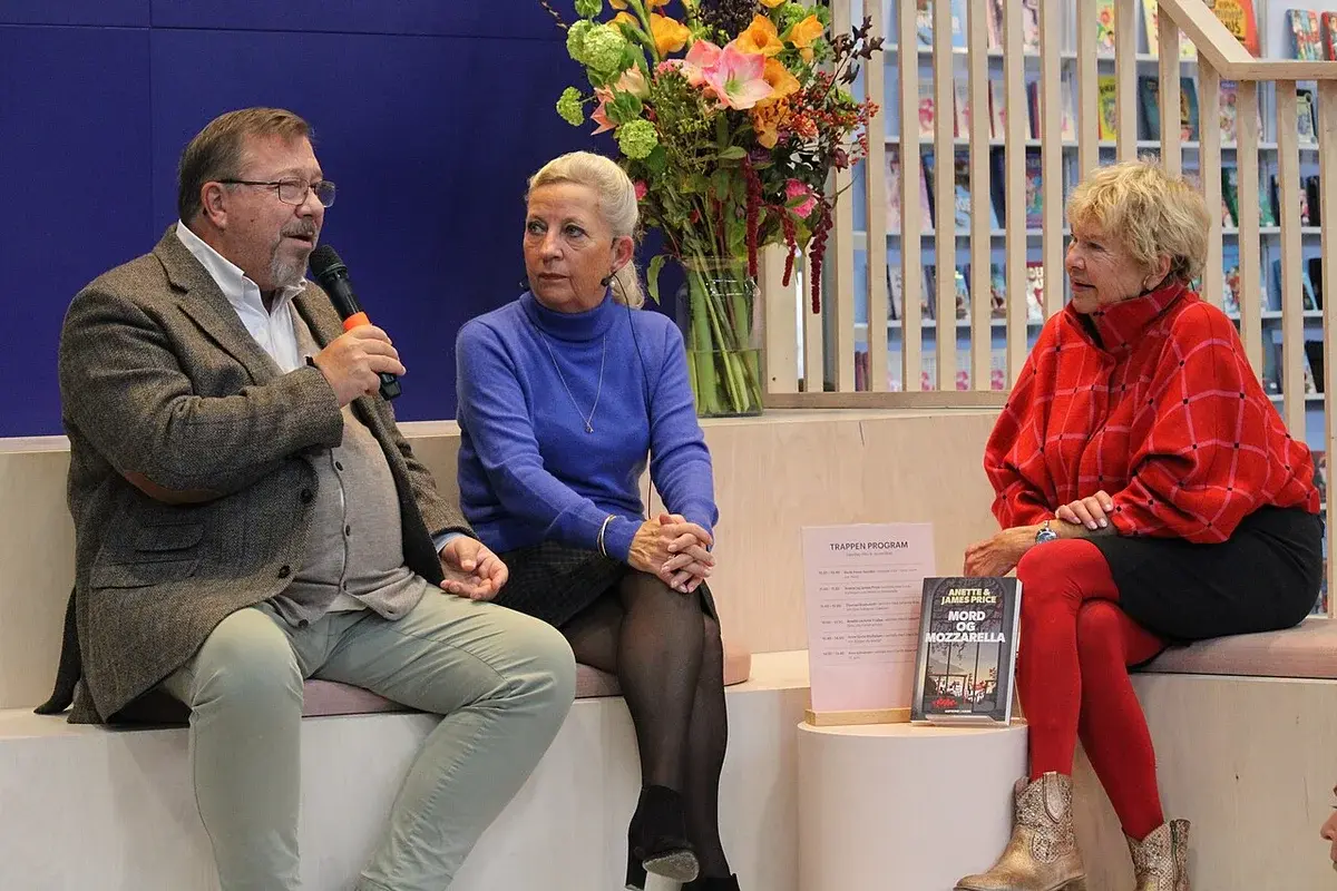 Three people seated on a stage at a book fair, with one speaking into a microphone.