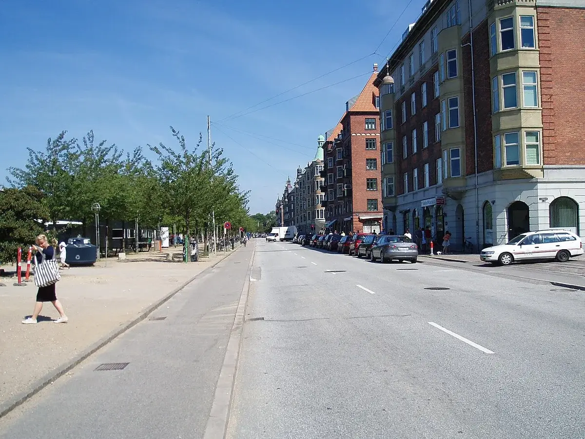 Street view of Islands Brygge in Copenhagen with buildings on one side and a sandy harborfront on the other.