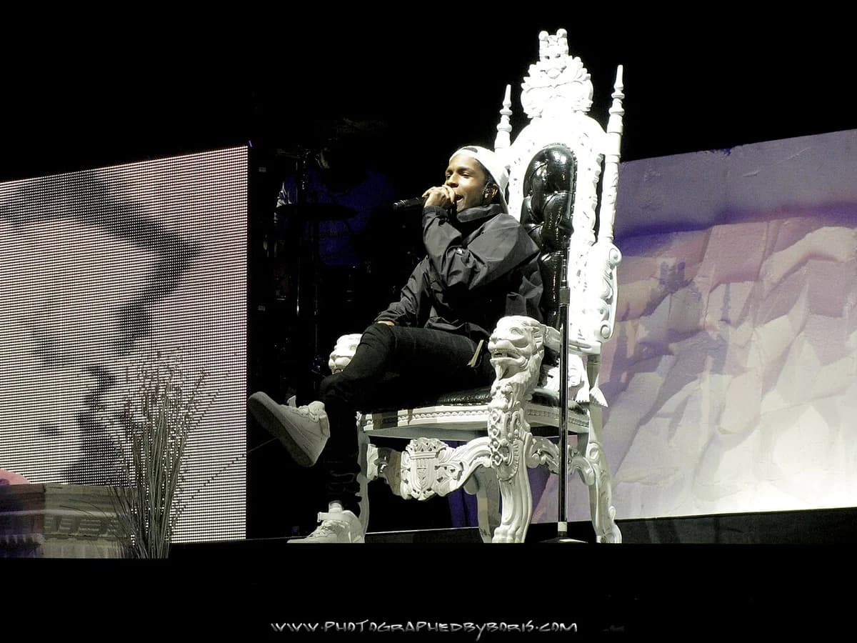 A man sits on an ornate throne and performs into a microphone on stage.