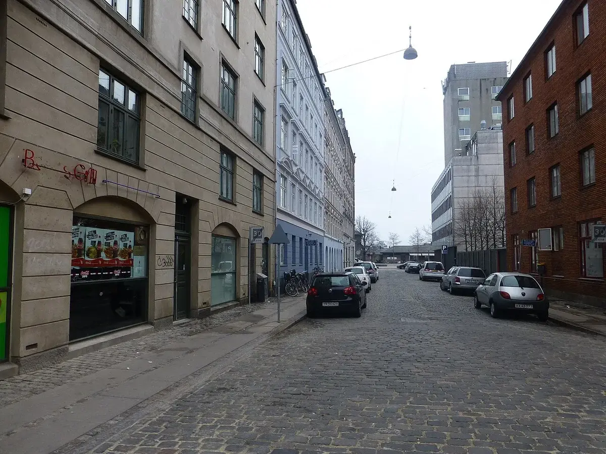 A cobblestone street lined with buildings and parked cars in Copenhagen.