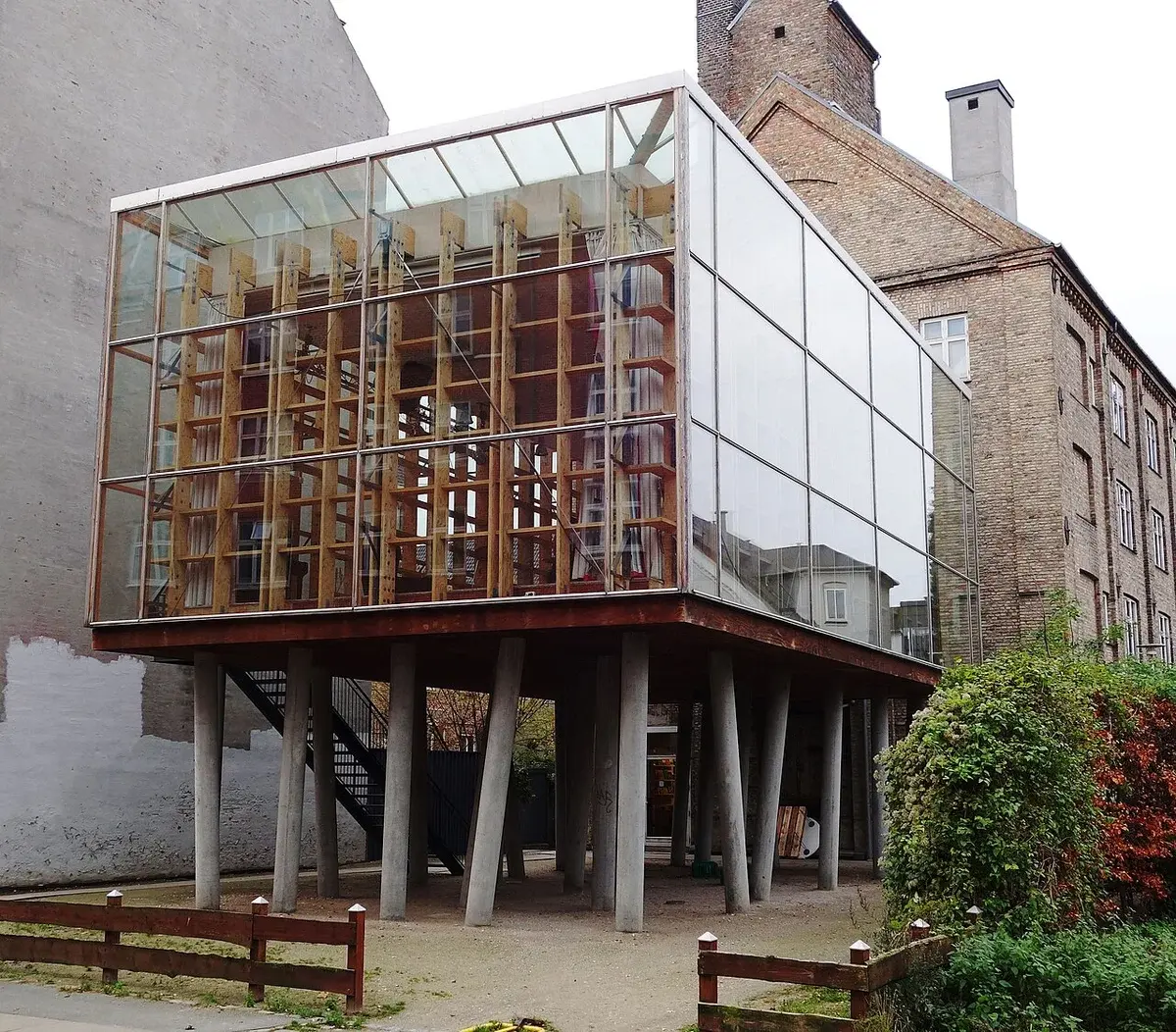 Modern glass building on angled concrete columns in an urban courtyard.