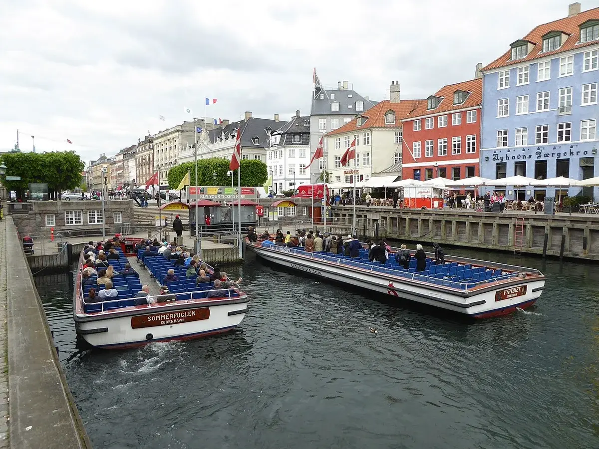 Two sightseeing boats in Nyhavn, Copenhagen, with passengers and colorful canal-side buildings.