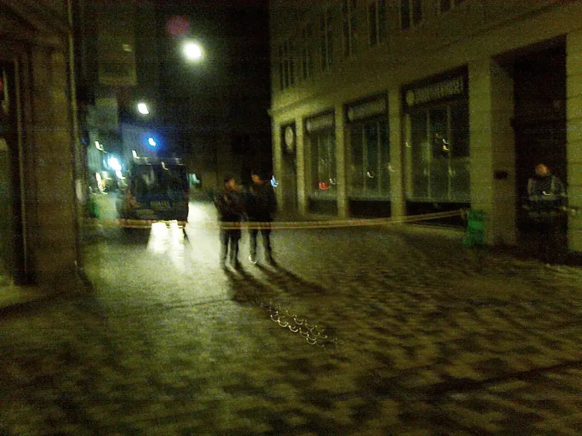 Police blockade on a cobblestone street at night with officers and police van