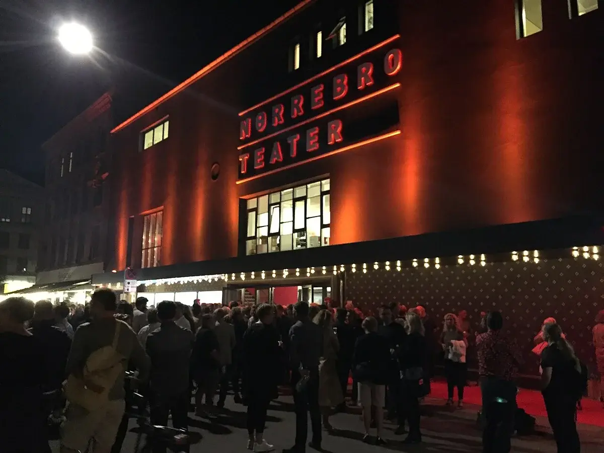 Night view of the Nørrebro Theatre building with people gathered outside.