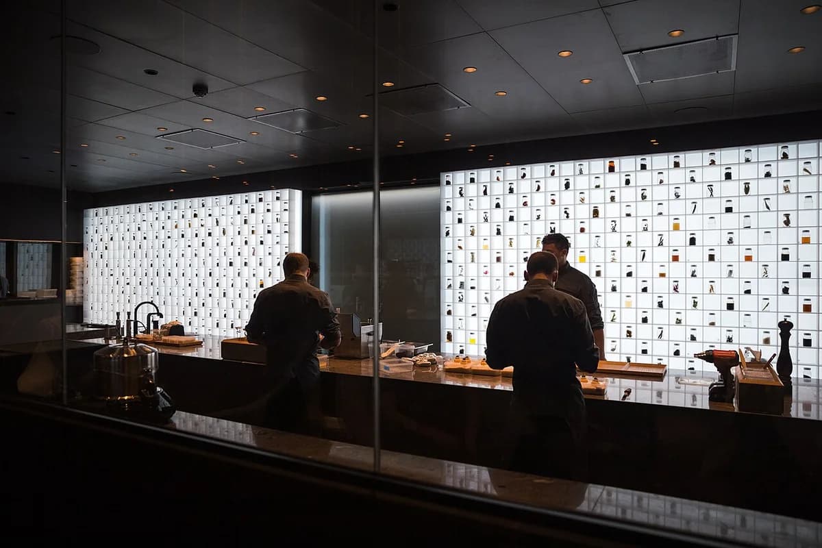 Dark modern restaurant interior with staff behind a counter and a wall of display compartments.