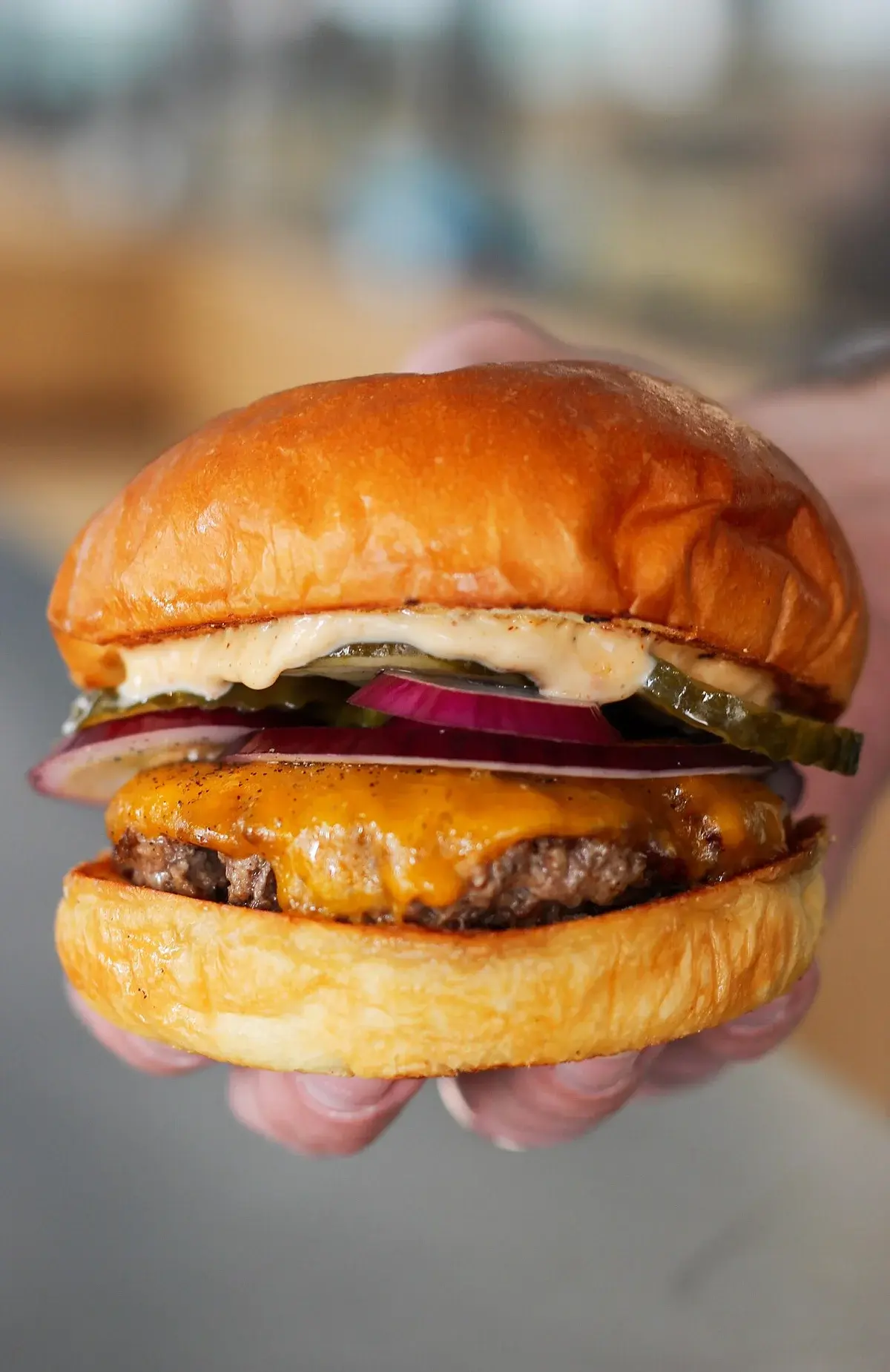 A close-up of a cheeseburger held in a hand.