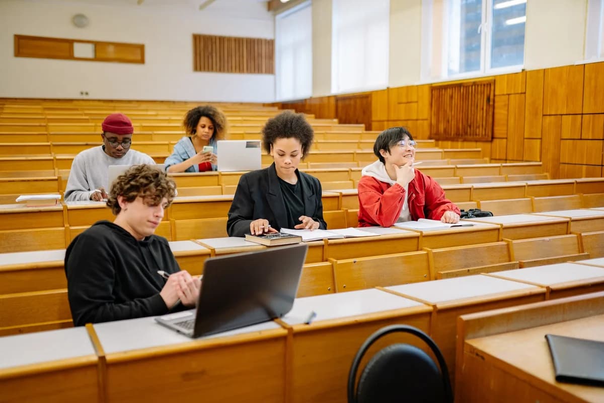Five college students studying in a lecture hall with laptops and books.