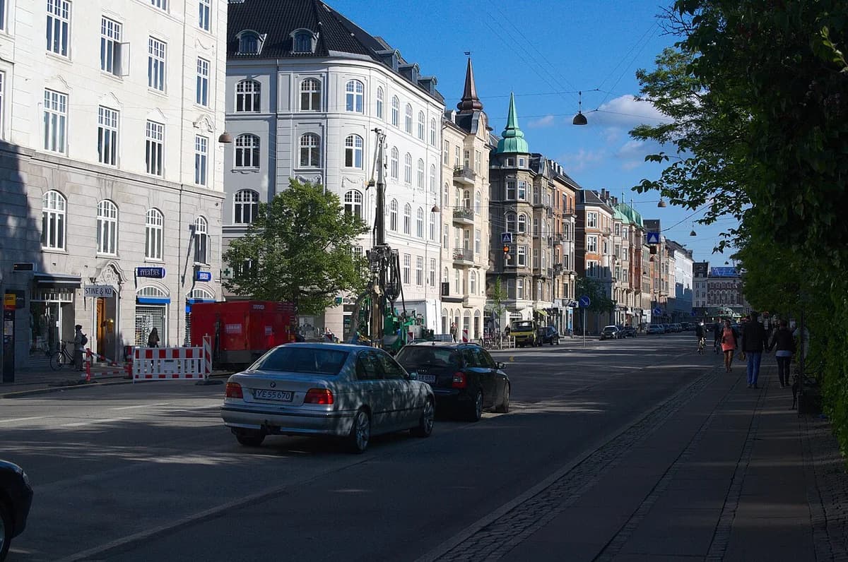 A Copenhagen street with historic buildings, cars, and pedestrians.