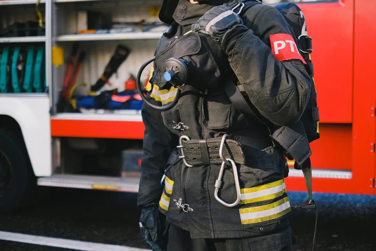 A firefighter in protective gear stands beside a fire truck.