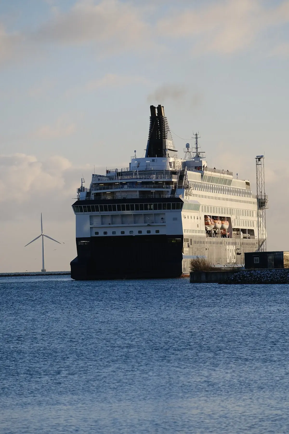 Large ferry in a harbor with a wind turbine in the background.