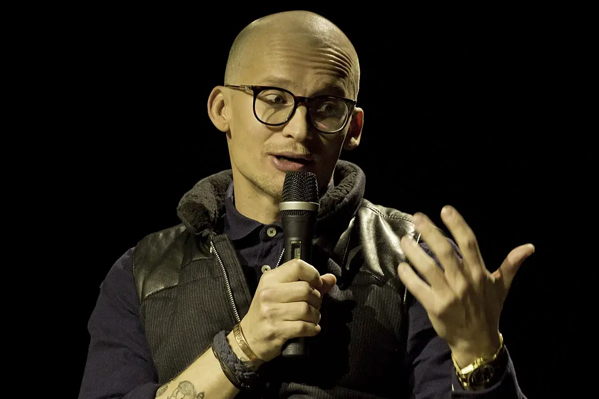 A man with glasses speaks into a microphone on stage.