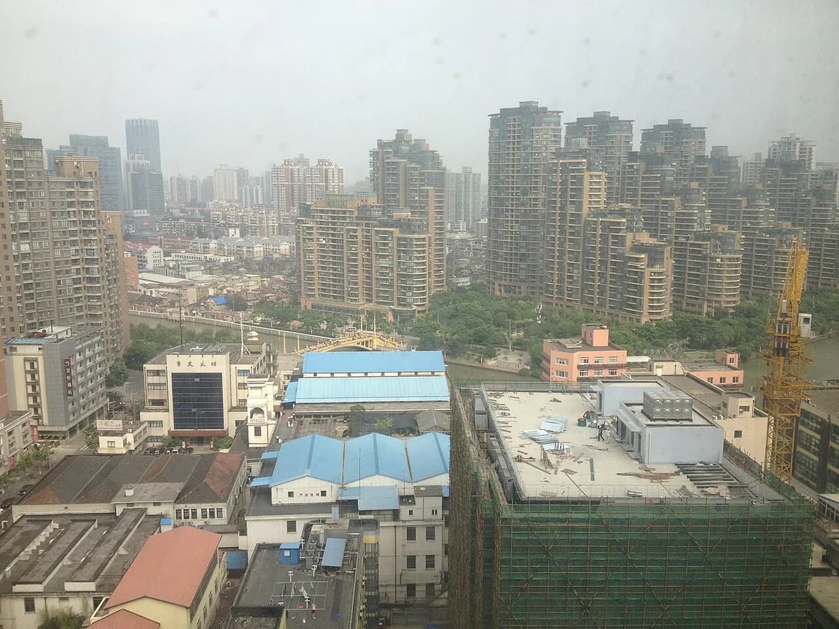 Hazy view of Shanghai skyline with apartment towers and construction cranes.