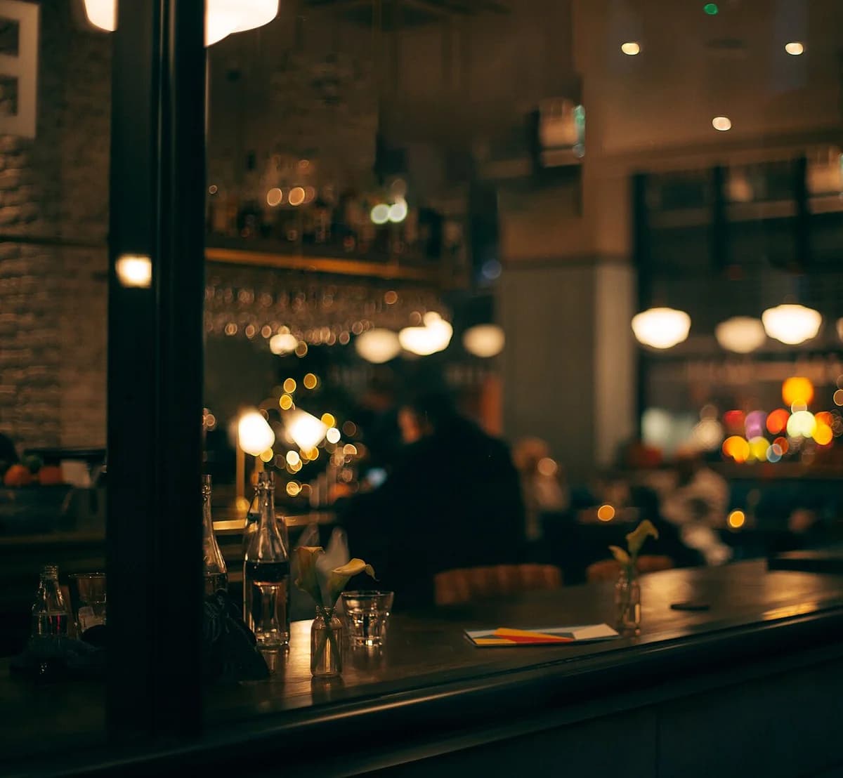 Dimly lit bar interior with warm lights and set tables at night.