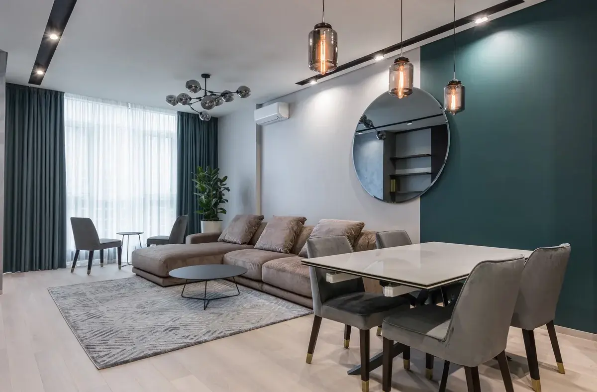 Modern living room with a sectional sofa, dining table, pendant lights, and teal accent wall.