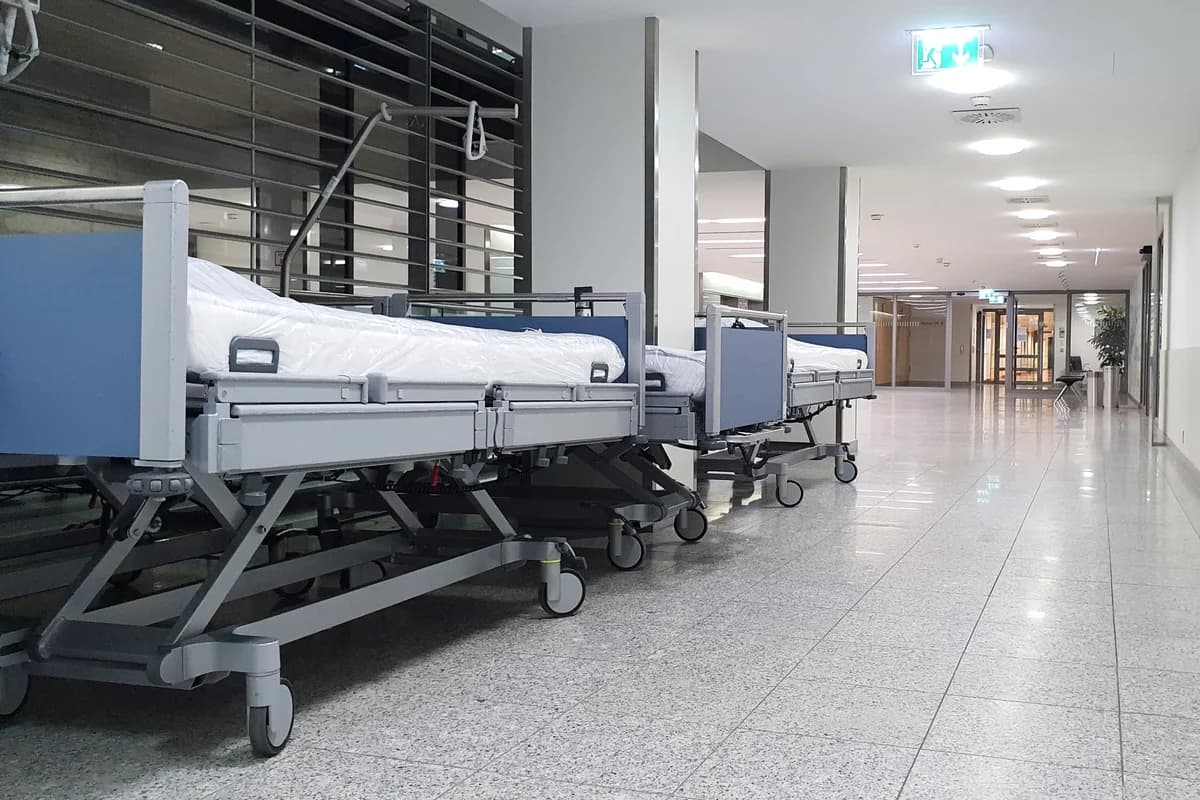 Empty hospital beds lined up in a bright corridor.