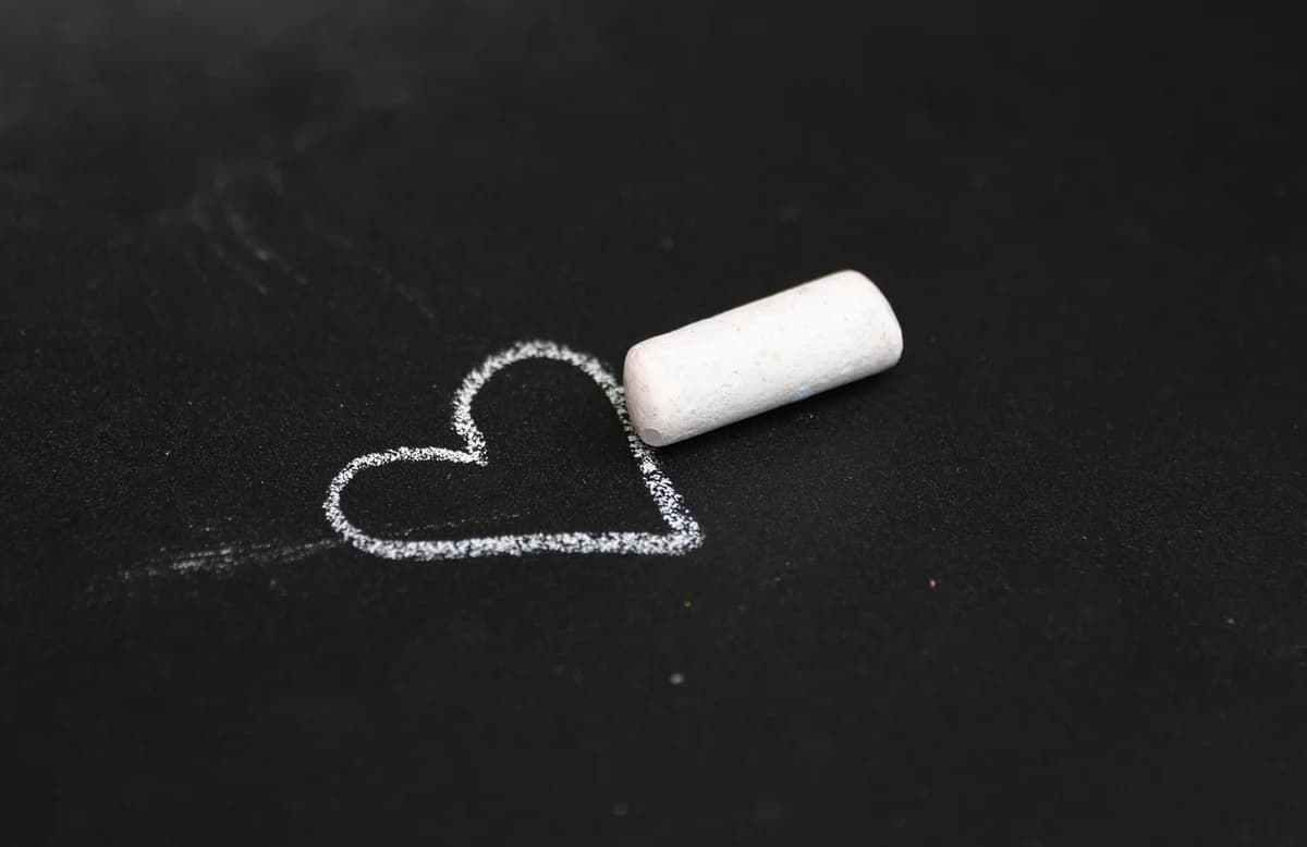 A heart drawn in chalk on a blackboard with a piece of white chalk nearby.