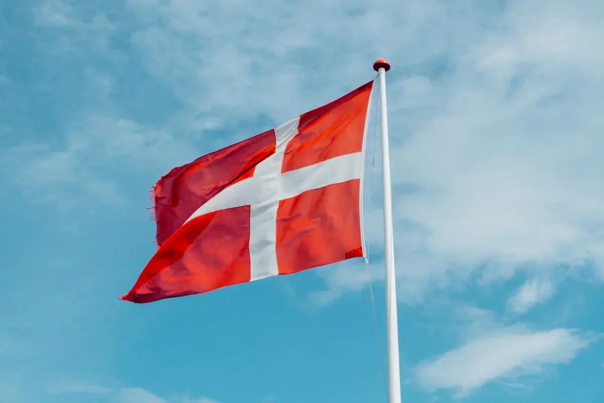 A Danish flag waving on a flagpole against a blue sky.