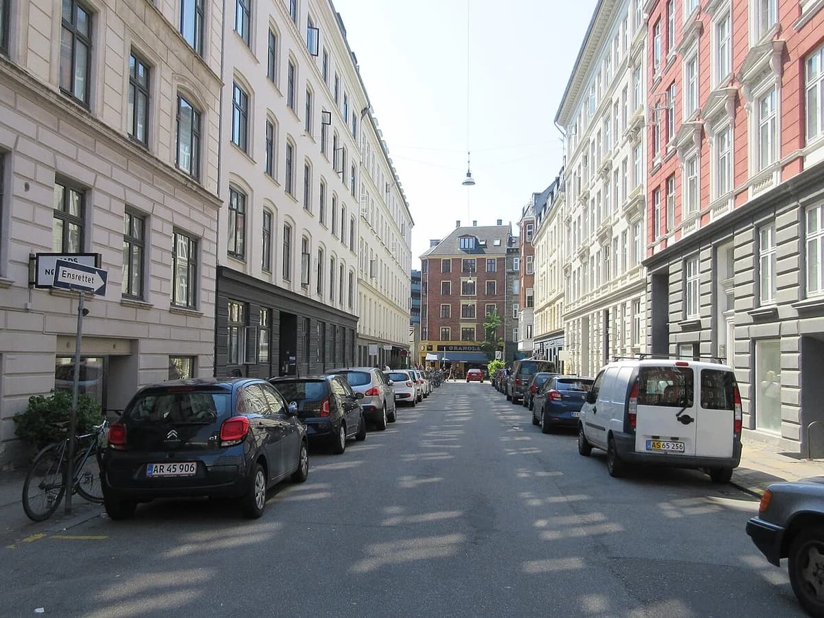 A quiet street with parked cars between tall apartment buildings in Copenhagen.