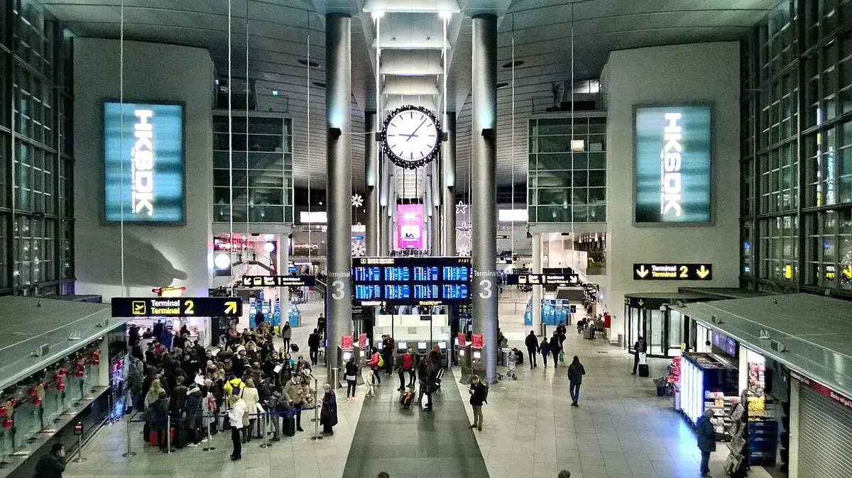 Busy airport terminal concourse with a large clock and travelers.