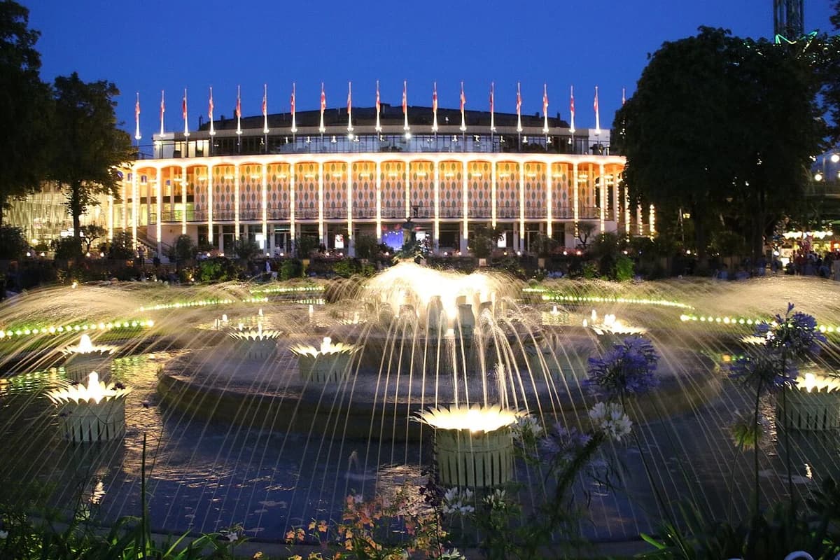 Illuminated fountain and building at Tivoli Gardens in Copenhagen at dusk.