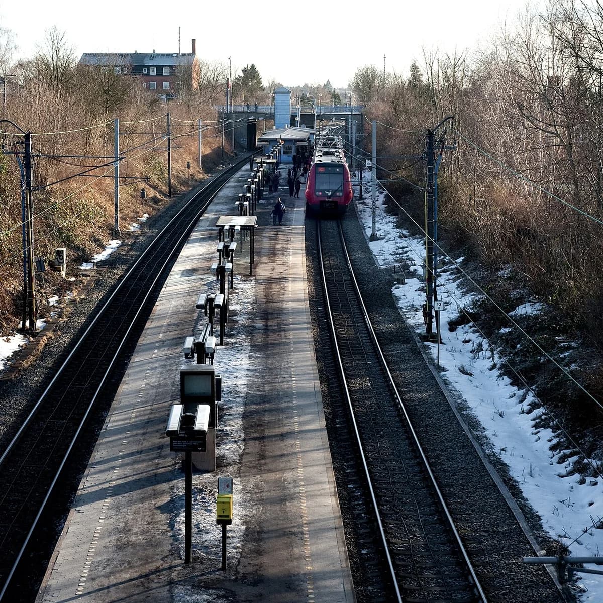 Exterior view of Husum S-train station in Copenhagen with a train at the platform.