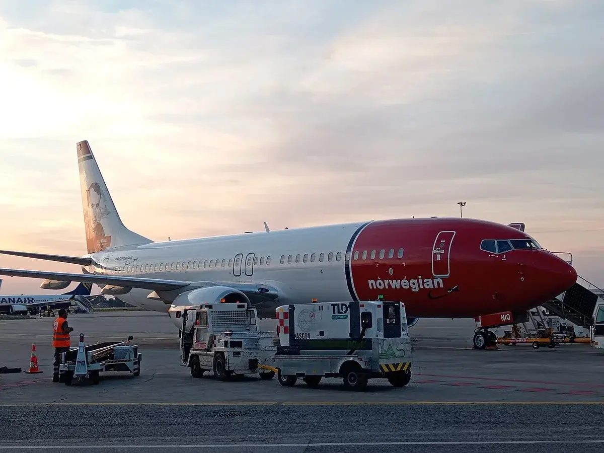 A Norwegian Air Shuttle plane on the tarmac in Bologna with ground vehicles nearby.