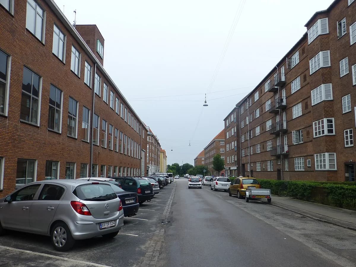 A quiet residential street with brick apartment buildings and parked cars in Copenhagen.