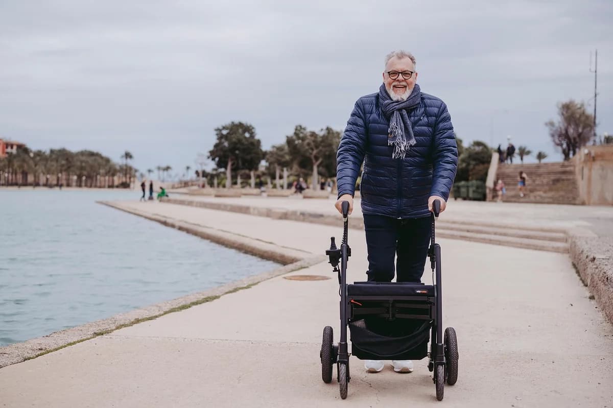 An older man uses a walker on a waterfront path.