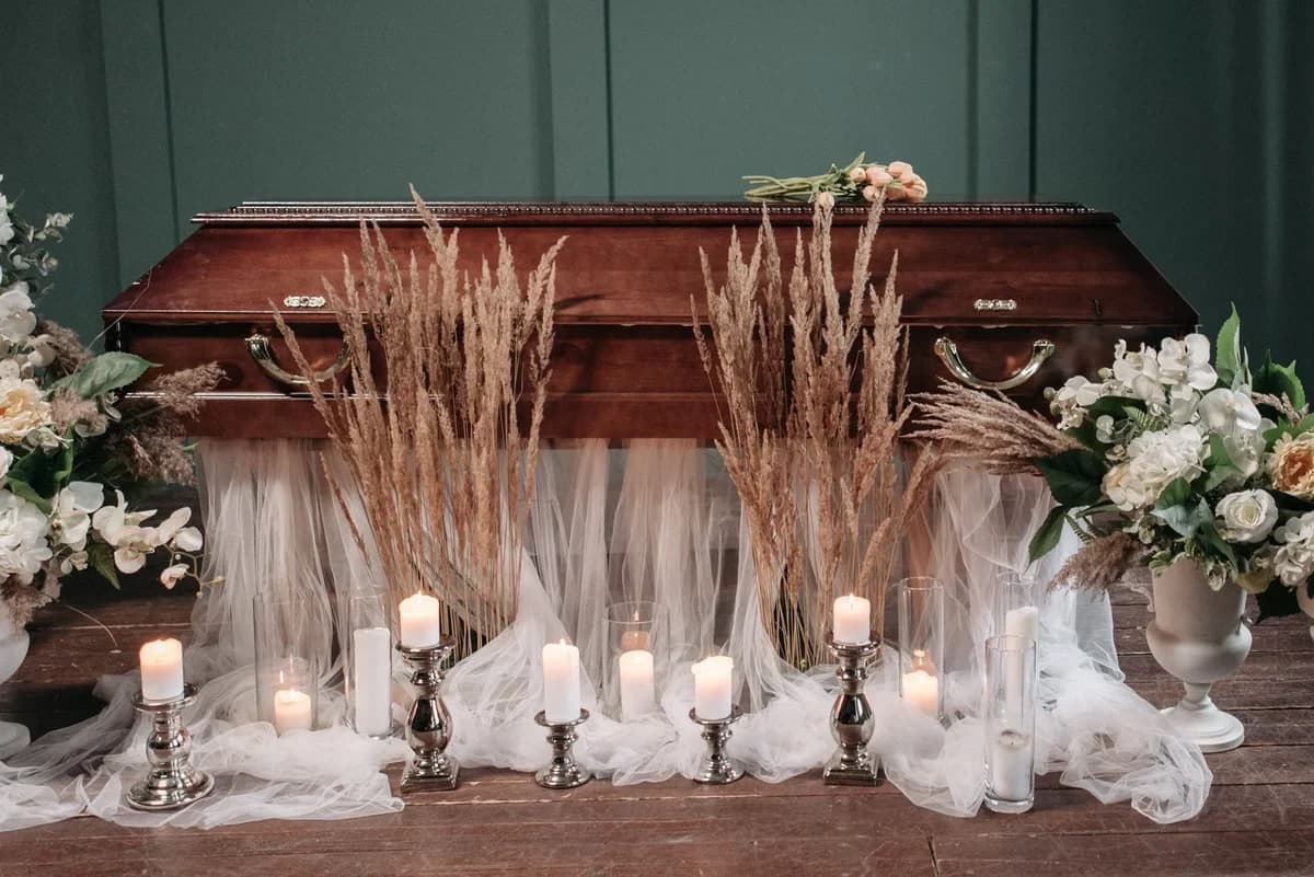 A decorated wooden coffin surrounded by candles, dried grasses, and floral arrangements.