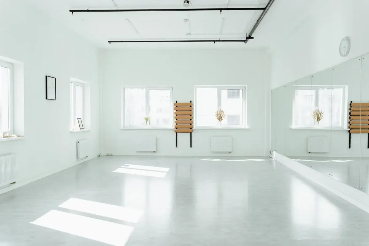 An empty, sunlit dance studio with mirrors and white walls.