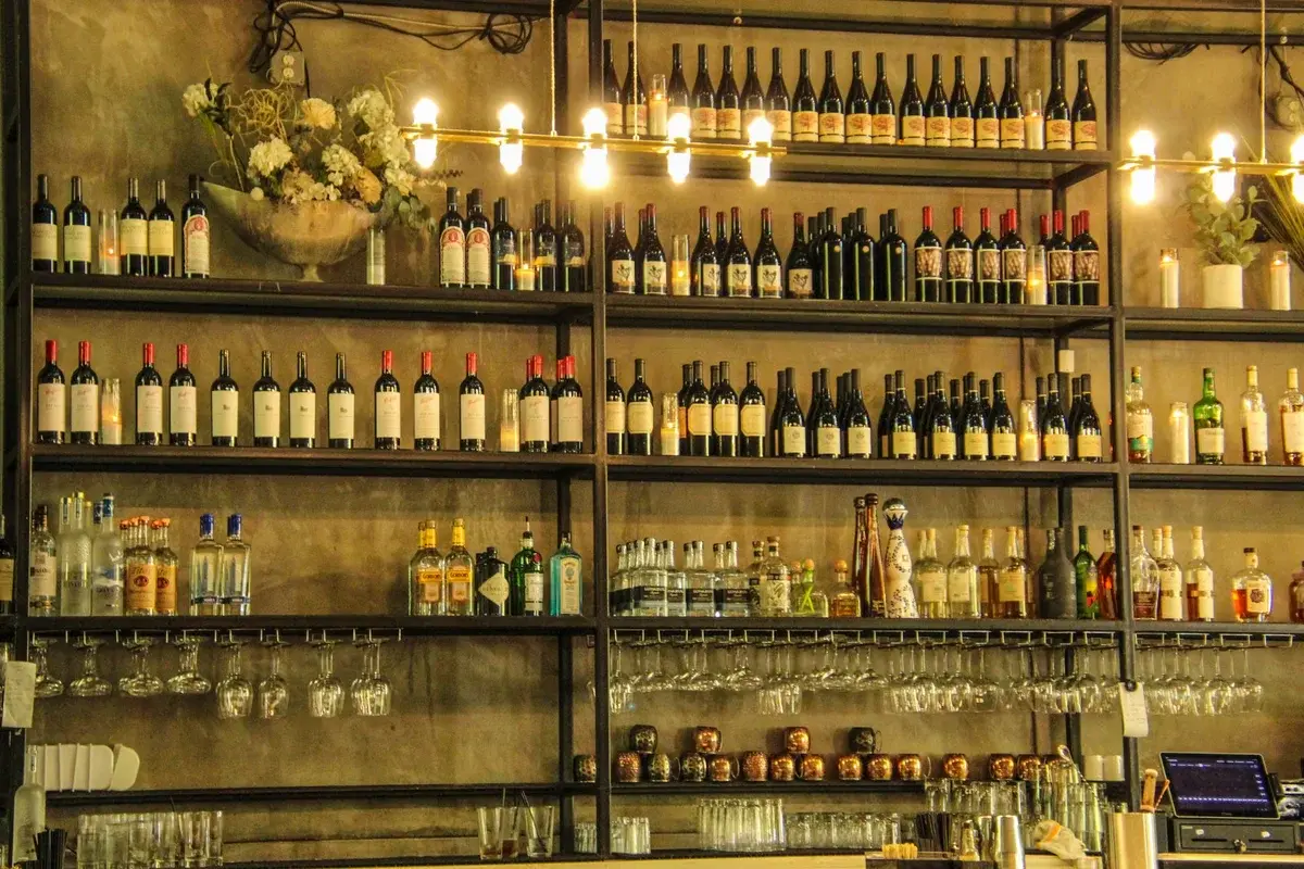 Bar shelf lined with wine and spirits bottles under warm lights